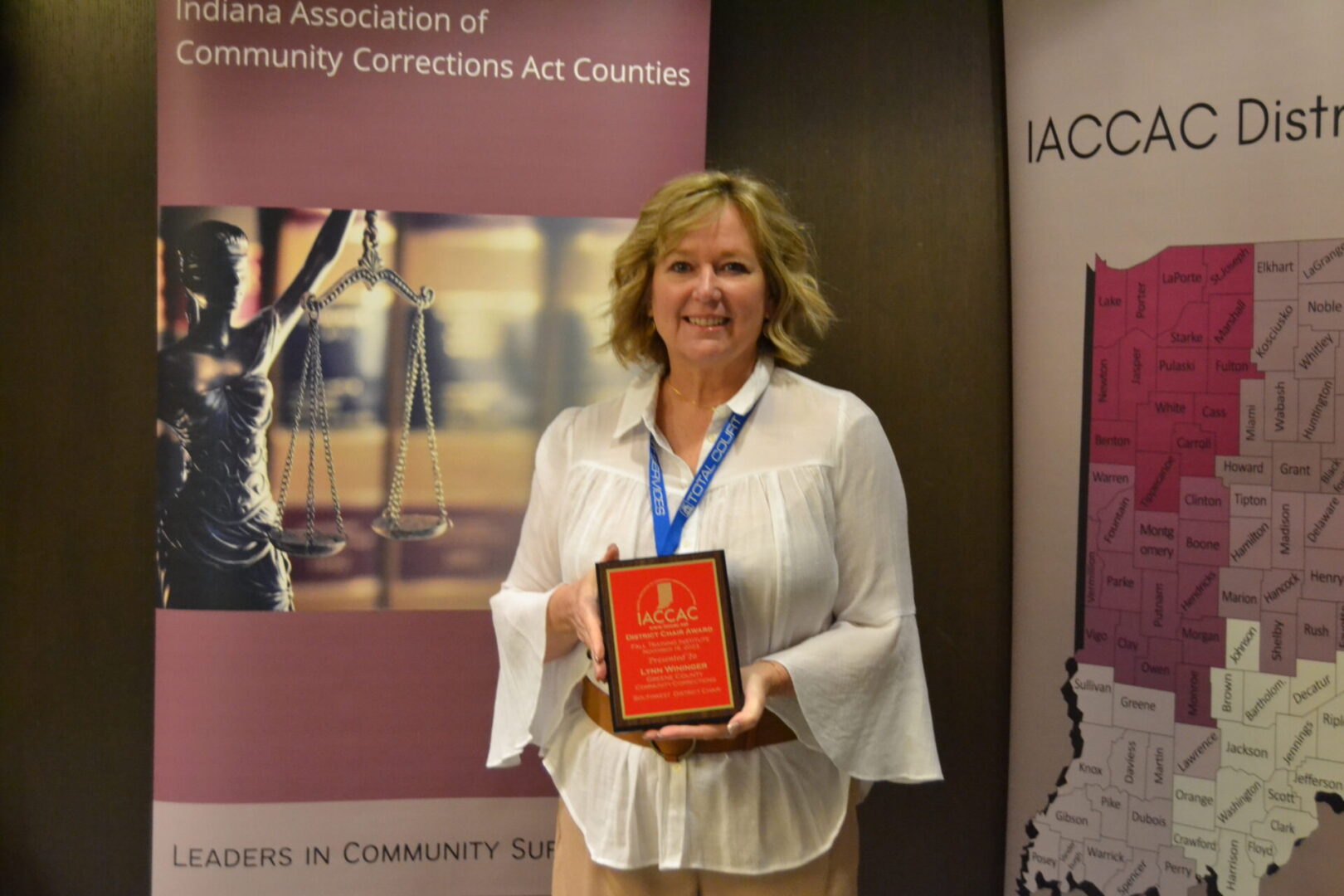 A woman holding an award in front of a banner.